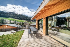 Eine moderne Holzterrasse mit Gartenmöbeln, mit Blick auf eine gebirgige Landschaft.