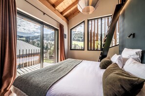 Ein Schlafzimmer mit einem großen Bett, Blick ins Freie und einer Holzbalkendecke.