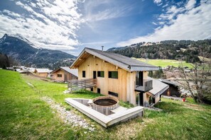 Eine Holzhütte mit Whirlpool und einer Terrasse, eingebettet in eine gebirgige Landschaft.