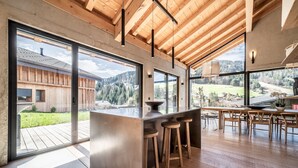 A modern kitchen with large windows, wooden beams, and a bar area. - NELCOTE - Design and luxury chalet with hot tub (Morzine)