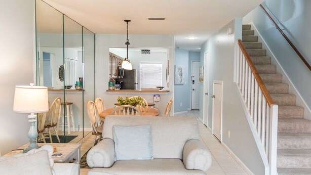 A living room with a sofa, chairs, a dining table, a kitchen area, and a staircase. - Ocean view townhouse with pools, tennis and so much more! SP 12230 (St. Augustine Beach)