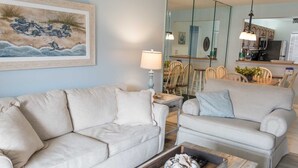 A living room with two sofas, a coffee table, a lamp, and a painting on the wall. - Ocean view townhouse with pools, tennis and so much more! SP 12230 (St. Augustine Beach)