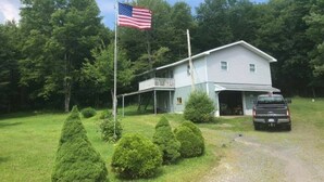 A two-story house with a garage, surrounded by well-maintained lawns and trees. - Cozy camp located in Elk County adjoining state game land. (Byrnedale)