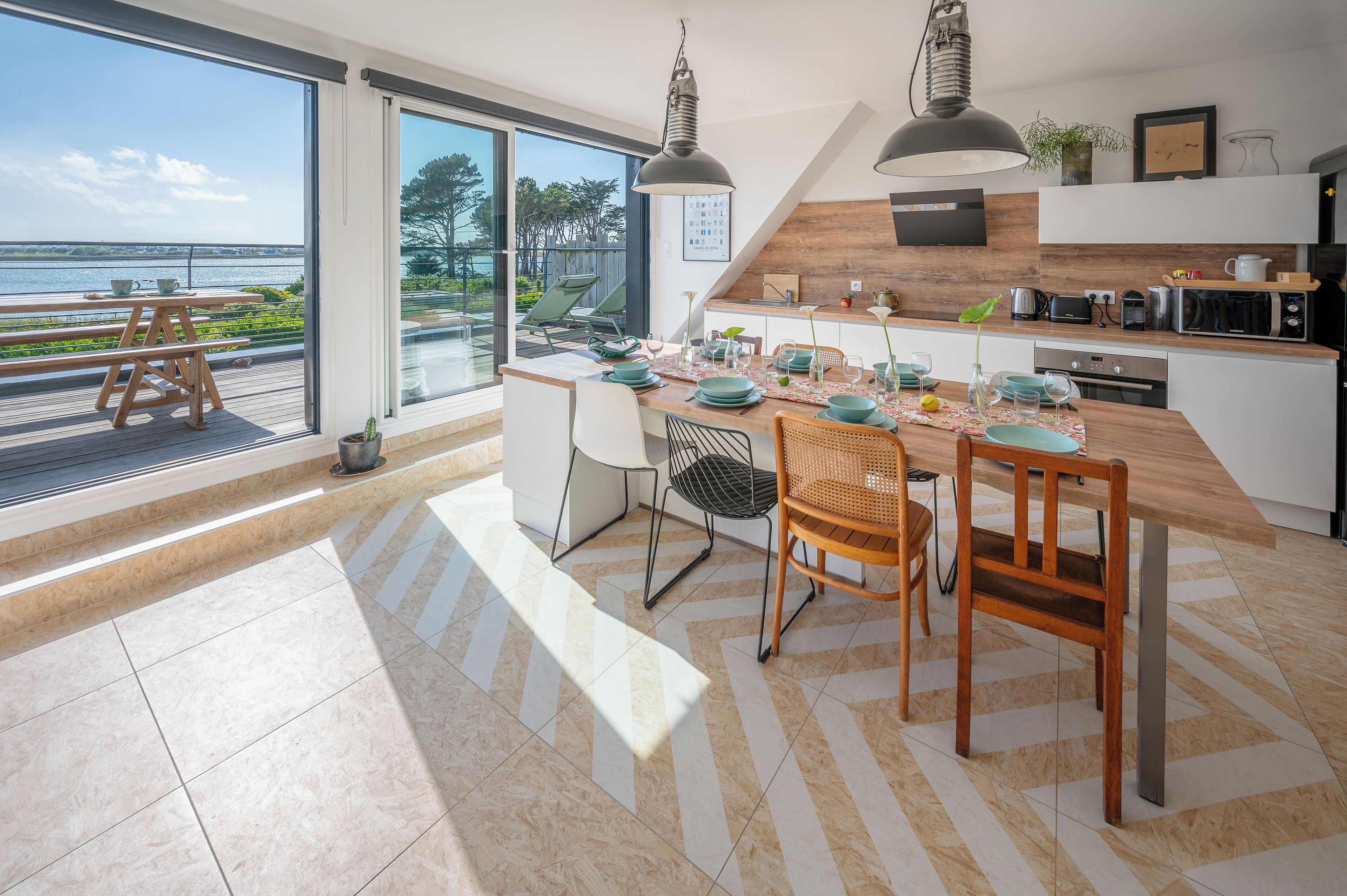 A modern kitchen with a large island, dining area, and a view of the sea.