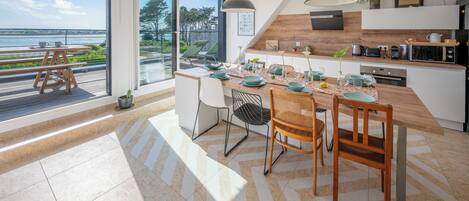 A modern kitchen with a large island, dining area, and a view of the sea.