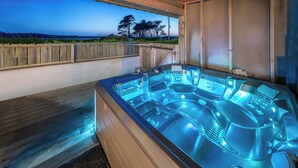 Un bain à remous doté de plusieurs jets, une terrasse en bois et une vue sur l’océan et les arbres.