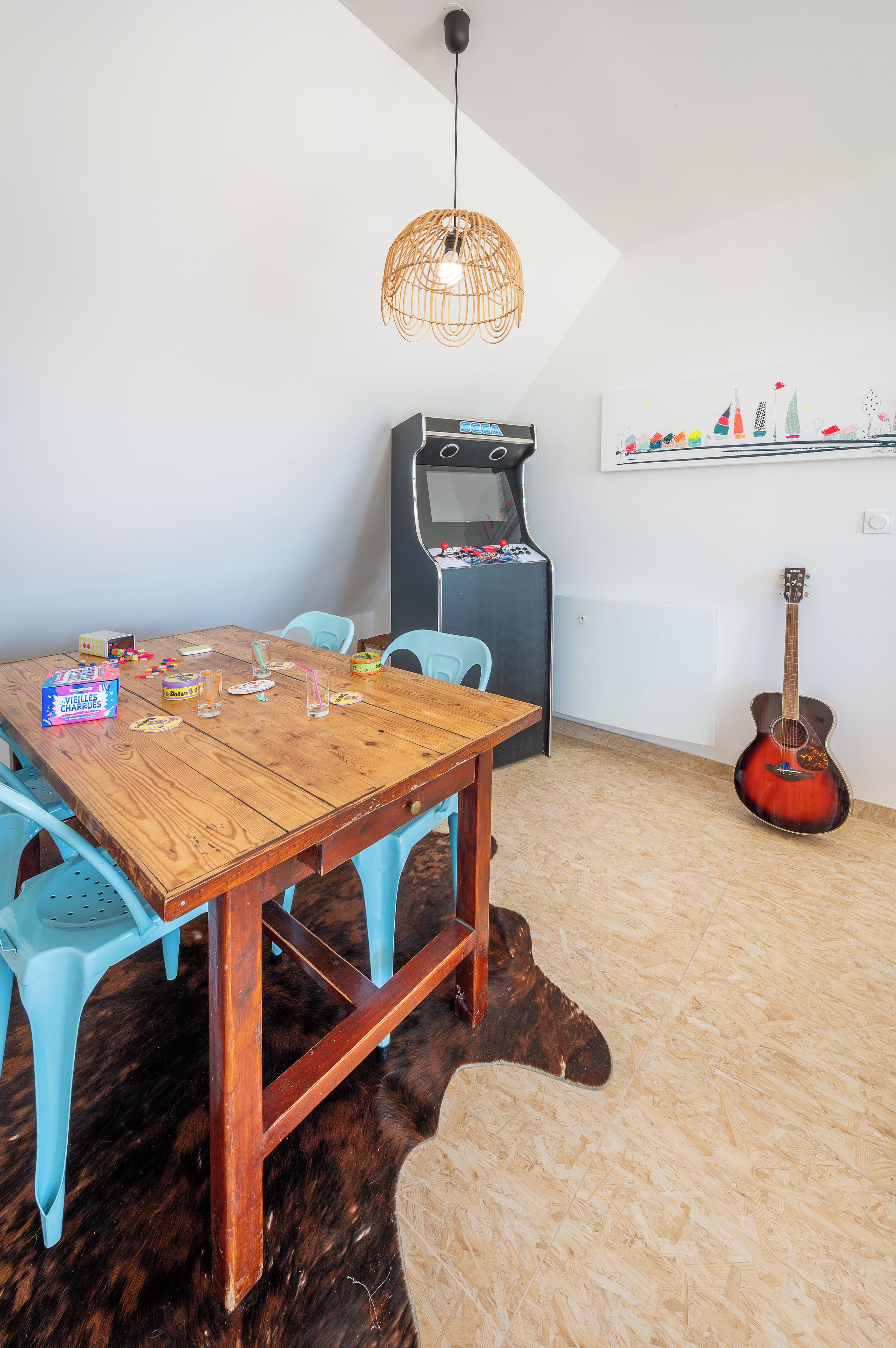Ein Essbereich mit einem Holztisch, blauen Stühlen, einer Gitarre und einem Retro-Arcade-Automaten.