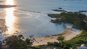 Un paysage côtier avec une plage, des affleurements rocheux et une maison dotée d’un jardin.