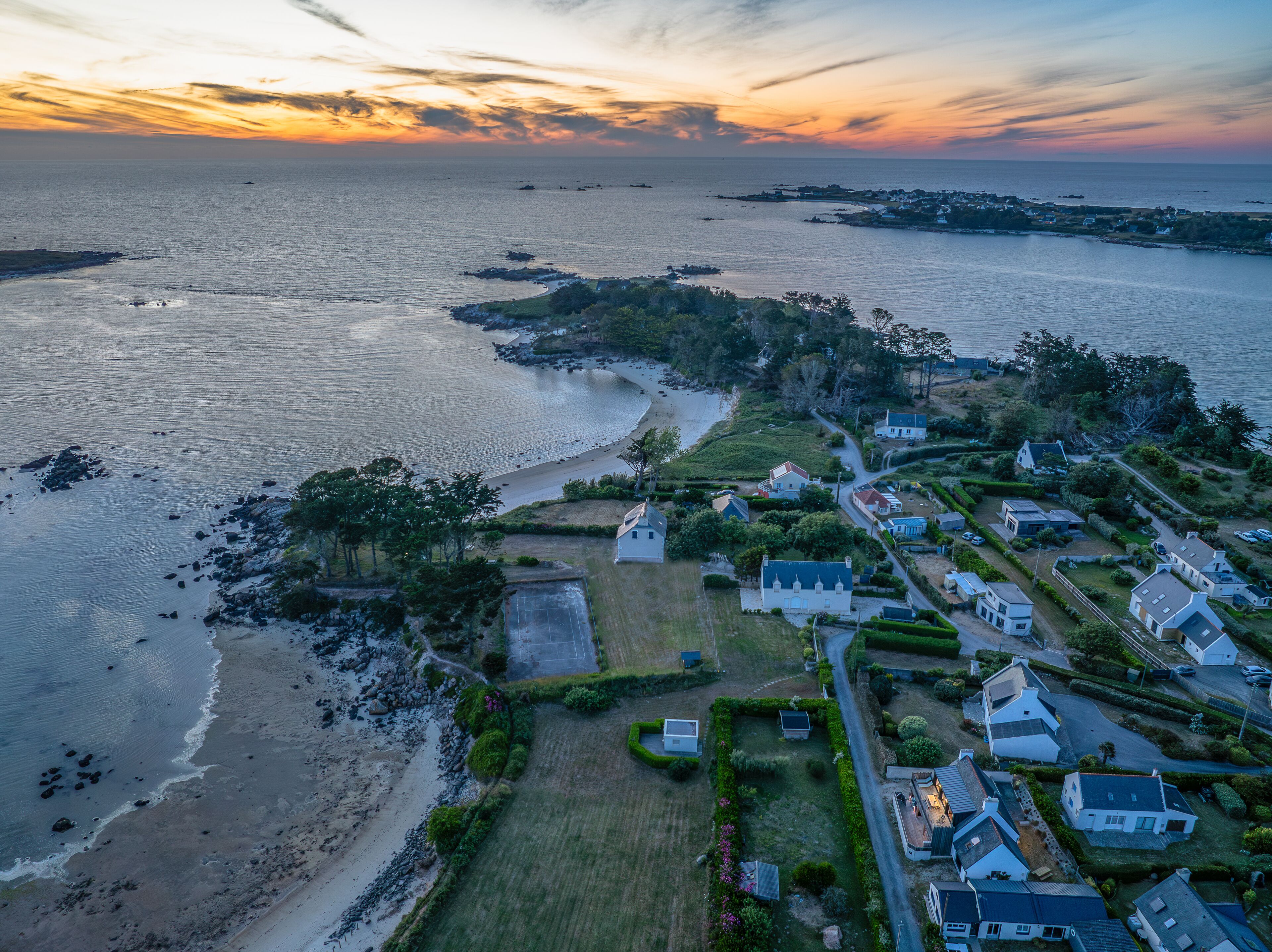 An aerial view of a coastal residential area with houses, a beach, and a small marina.