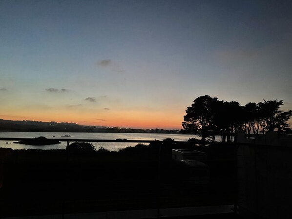 A sunset view over a body of water with silhouettes of trees and a distant shoreline.