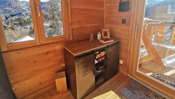 Een houten hut met een kleine kitchenette, een hangende tas en uitzicht op besneeuwde bergen.
