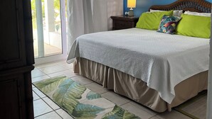 Een slaapkamer met een bed, gordijnen, een nachtkastje, een lamp en een plafondventilator.