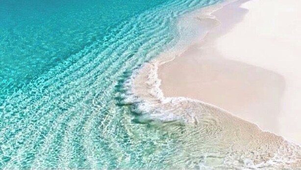Een strand met helder turquoise water en wit zand.