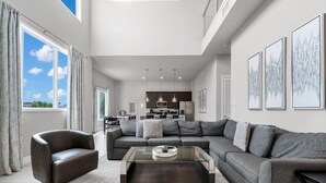 A spacious living room with a modern sofa, a glass coffee table, and a view of the kitchen in the background.