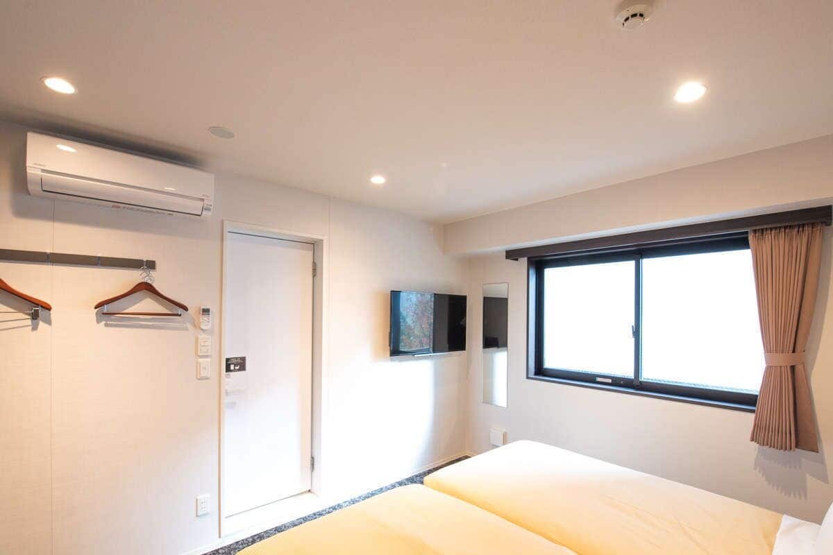 Quarto de hotel com cama, televisão, janela com cortinas, ar condicionado e porta.