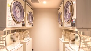 A laundry room with multiple washing machines and dryers, arranged in a row with baskets on the floor. - Hotel Livemax Hakata-ekimae (Fukuoka)