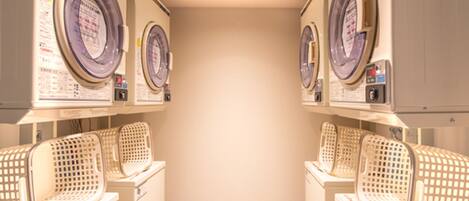 A laundry room with multiple washing machines and dryers, arranged in a row with baskets on the floor.