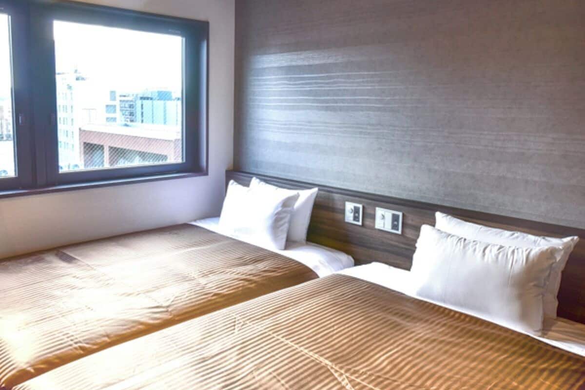 Quarto de hotel com duas camas, uma janela grande e vista para edifícios.