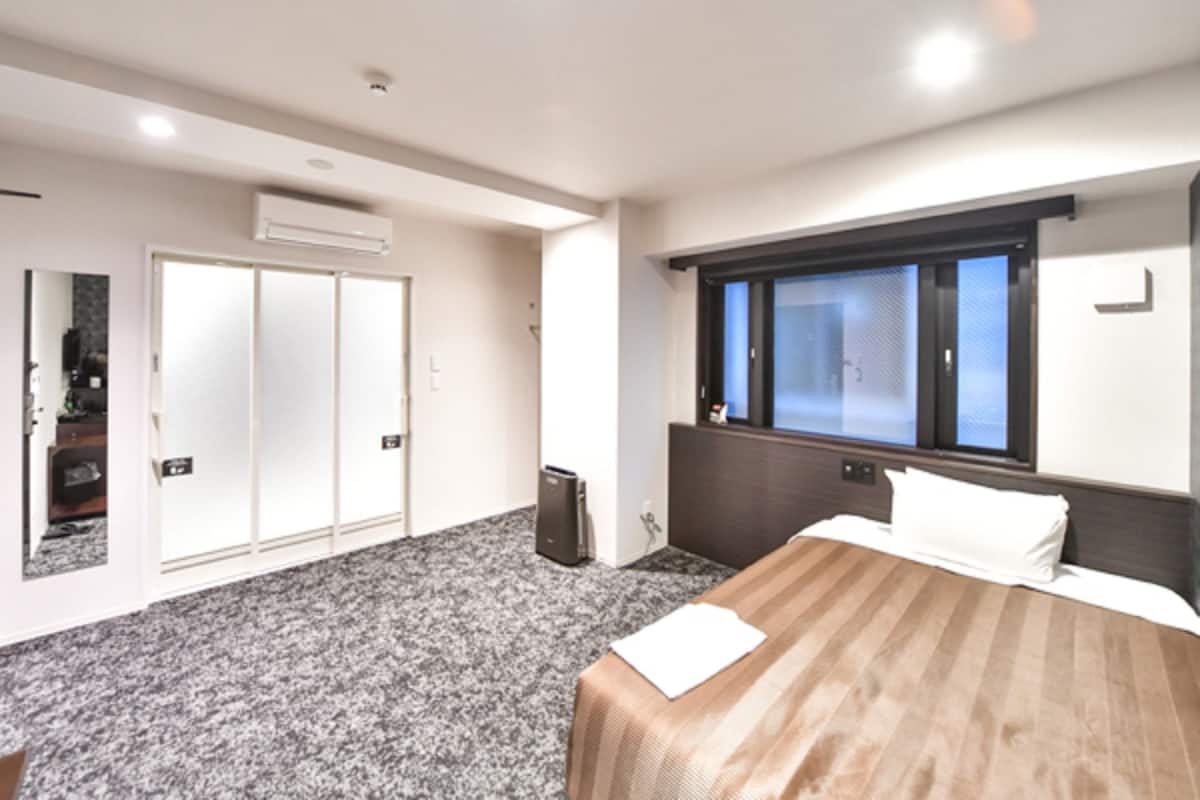 Quarto de hotel com uma cama, janela, guarda-roupa e uma pequena escrivaninha.