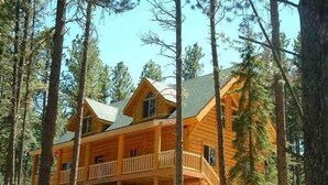 A multi-story log cabin with a balcony on the second floor, surrounded by tall pine trees. - Arrow Lodge (Lead)