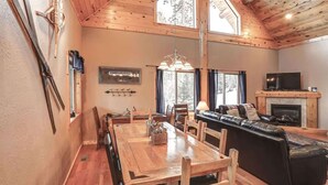 A cozy cabin interior with a wooden dining table, a sofa, and a fireplace. - Arrow Lodge (Lead)