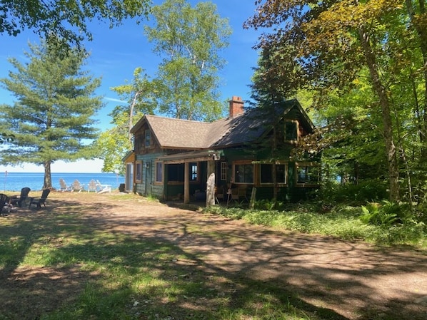 Een rustieke hut met een ruim terras, omringd door bomen en uitzicht op het water.