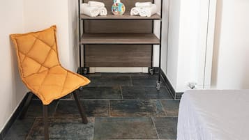 A room with a tufted orange chair, a shelf with folded towels, and a bed with a white cover.