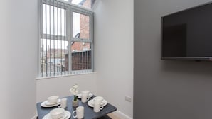 Un comedor con una mesa dispuesta para cuatro, una ventana con rejas y un televisor montado en la pared.