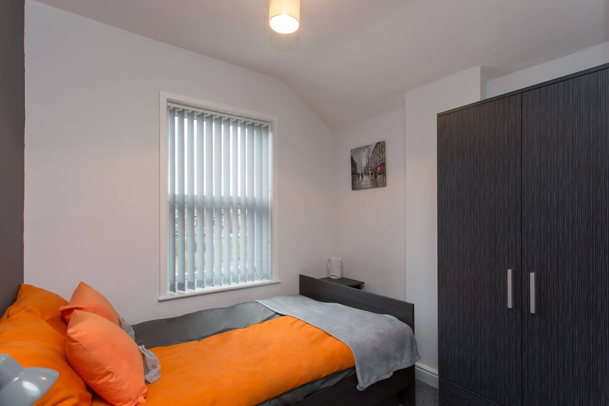 Une chambre à coucher avec un lit, une fenêtre avec des stores, une armoire et une table de chevet.