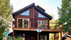 A two-story wooden house with a balcony, surrounded by a garden with various plants and flowers. - 2BR 2BA In Town, Pet Friendly, Fenced Yard, Walkable, Large Deck (Crested Butte)