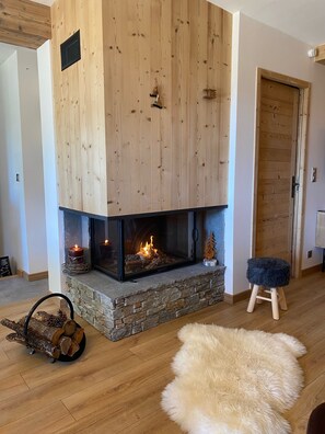 Un salon chaleureux avec une cheminée en pierre, des boiseries, un tapis moelleux et un petit tabouret.
