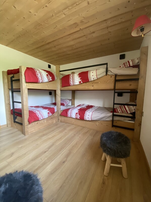 A bunk bed room with wooden floors and a small stool.