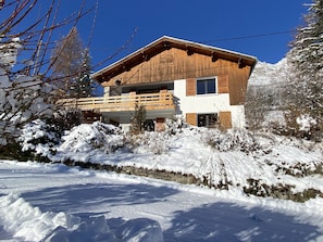 Un chalet en bois à deux étages, doté d’un balcon, entouré d’un paysage enneigé et d’arbres.