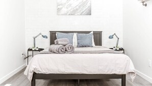 A neatly made bed with a white bedspread, two pillows, and rolled towels on a dark wooden bed frame. - Renovated 2story(7C) OSU/ExpoCenter/Central ❤NearEVERYTHING (Columbus)