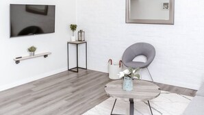 A modern living room with a grey chair, a round coffee table, a TV, and a small side table with a plant. - Renovated 2story(7C) OSU/ExpoCenter/Central ❤NearEVERYTHING (Columbus)