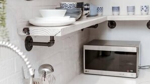 A kitchen with white marble countertops, a microwave, hanging utensils, and shelves with dishes and cups. - Renovated 2story(7C) OSU/ExpoCenter/Central ❤NearEVERYTHING (Columbus)