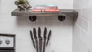 A kitchen with white tiled walls, a marble countertop, a stove, and two floating shelves with books and a small plant. - Newly Renovated (9E) OSU/ExpoCenter/Central ❤NearEVERYTHING (Columbus)