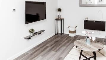 A modern living room with a flat-screen TV mounted on the wall, a small round table with a vase, and a wooden bench with a plant.