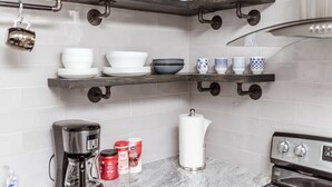 A kitchen with white tiled walls, a marble countertop, and a coffee maker. There are shelves with dishes and cups, and a kettle on the counter. - Newly Renovated (9E) OSU/ExpoCenter/Central ❤NearEVERYTHING (Columbus)
