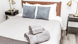 A neatly made bed with grey and white linens, two grey pillows, and a pair of rolled towels on the bed. - Newly Renovated (9E) OSU/ExpoCenter/Central ❤NearEVERYTHING (Columbus)