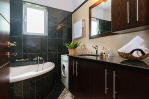 A modern bathroom with a freestanding bathtub, a sink with a mirror above, a washing machine, and a potted plant. - Stunning Comfortable Family House in Chania (Chania)