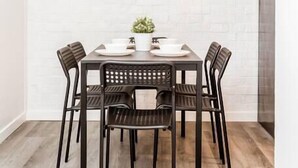 Un espace repas avec un mur en briques blanches, un luminaire suspendu aux formes géométriques et deux tableaux encadrés.
