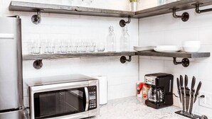 Une cuisine équipée d’un réfrigérateur en acier inoxydable, d’un four à micro-ondes, d’une machine à café et d’étagères contenant de la vaisselle et des assiettes.