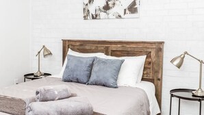 Un lit bien fait, avec une tête de lit en bois, deux lampes de chevet et une œuvre d’art encadrée accrochée au mur.