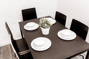A dining table for four is set against a brick wall, accompanied by four chairs and a central vase with a plant.