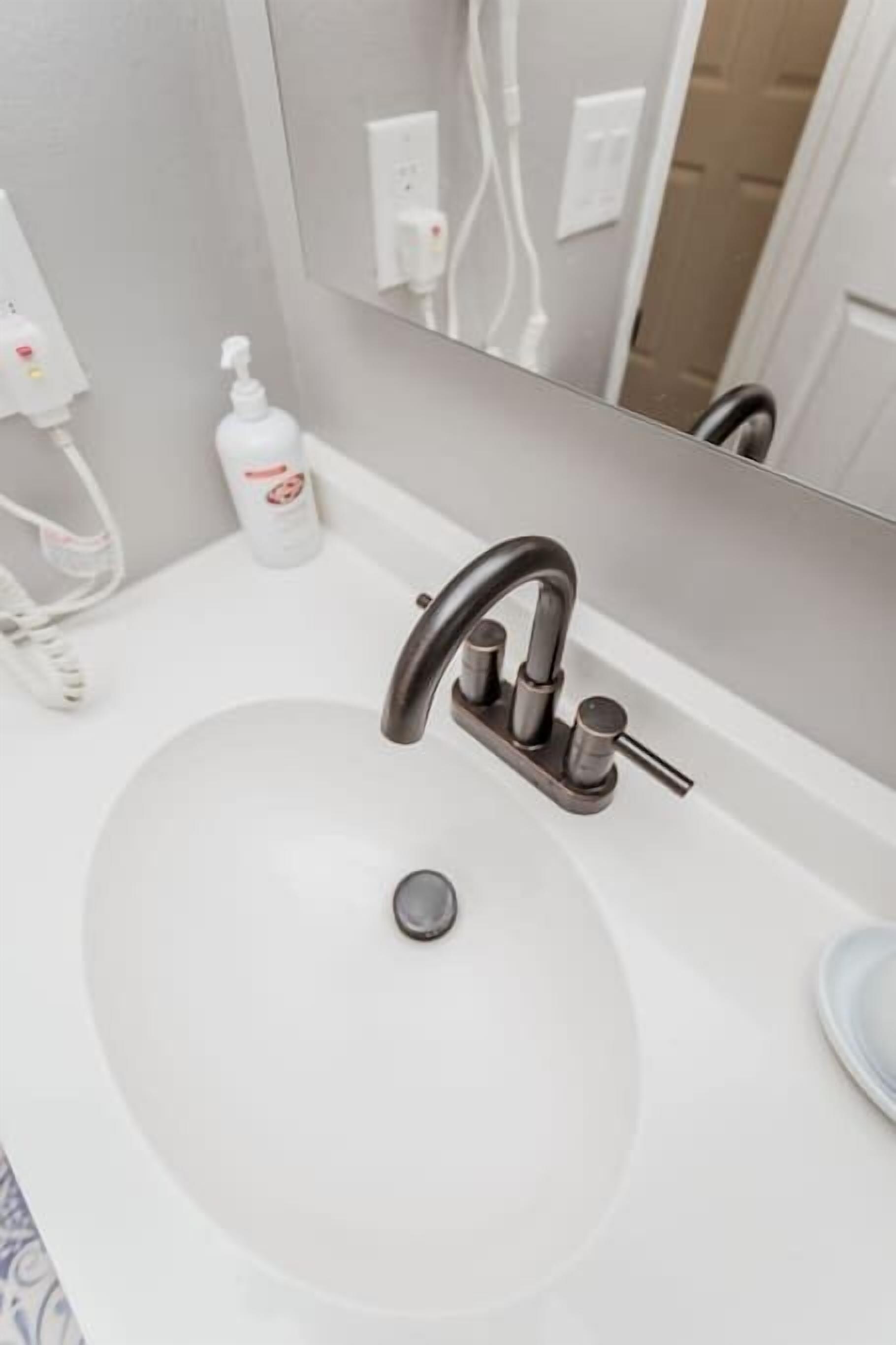 A modern bathroom with a white sink, a dark faucet, and a mirror above it.