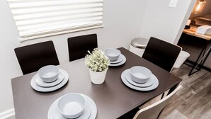 A dining table with six plates and bowls, a potted plant, and black chairs.