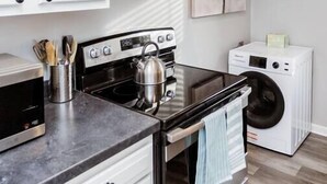 A modern kitchen with stainless steel appliances, white cabinetry, and a washing machine.