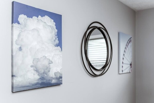 Una pared con un cuadro de nubes, un espejo redondo y una fotografía en otro marco.