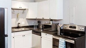 A modern kitchen with white cabinets, stainless steel appliances, and a striped rug.